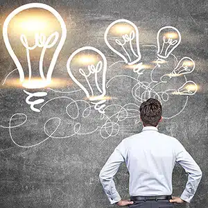 Idea concept with businessman looking at illuminated lightbulb sketches on chalkboard background
