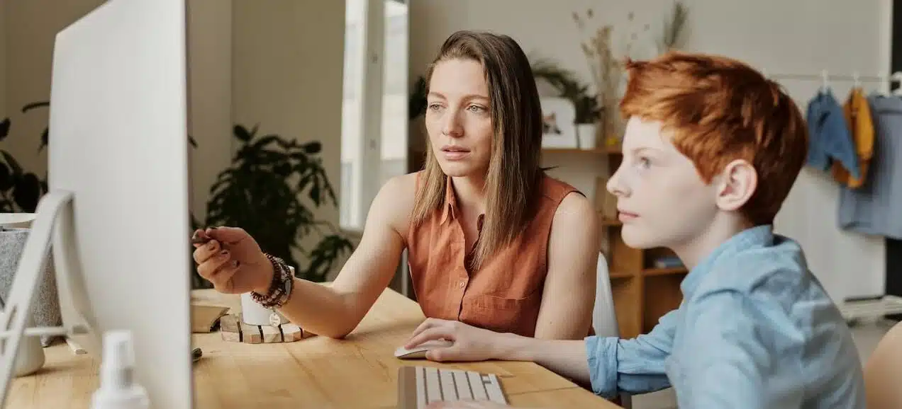 A teacher teaching a boy responsible digital citizenship on his desktop computer