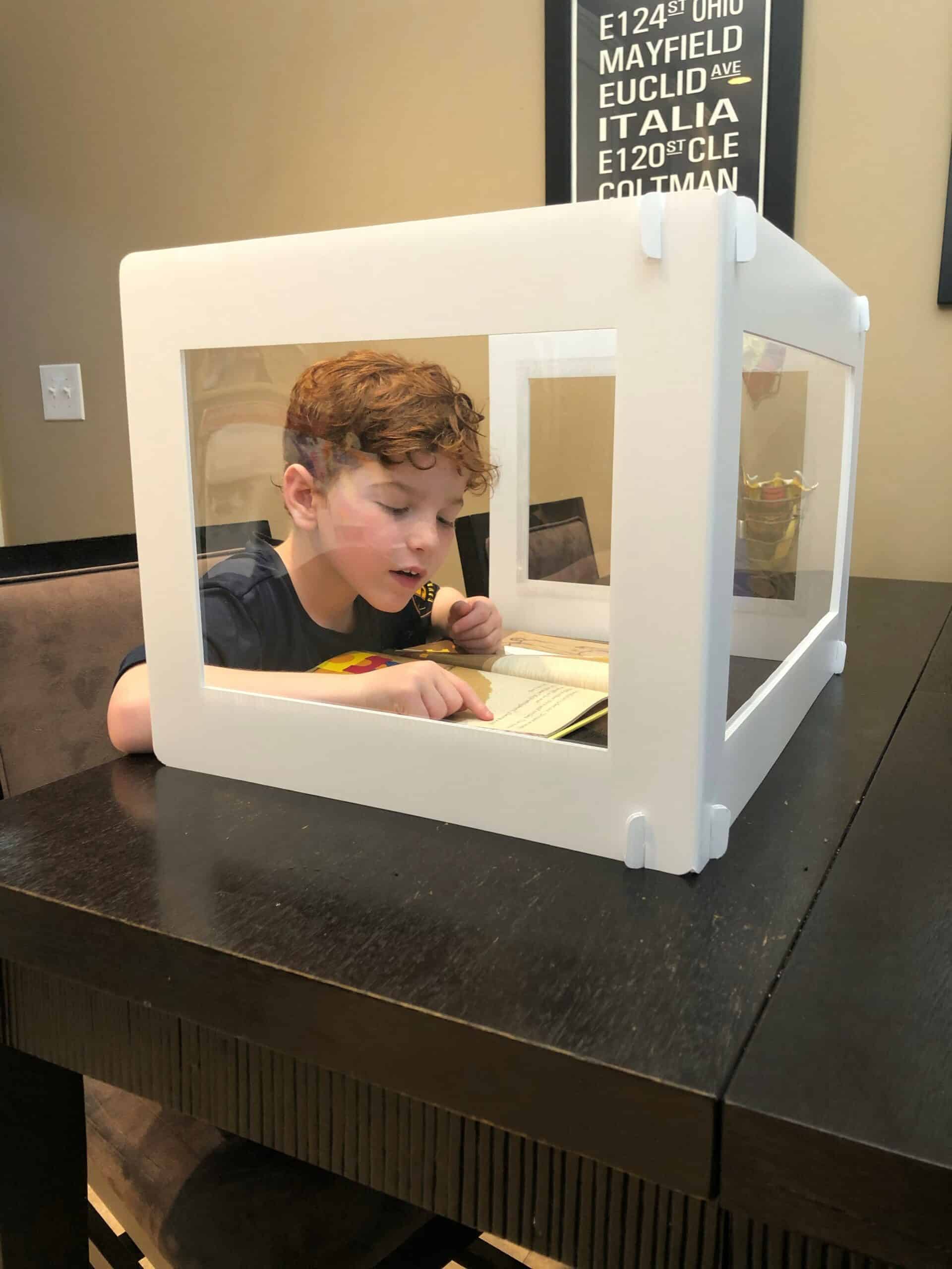 A child sitting at a table with a desk shield