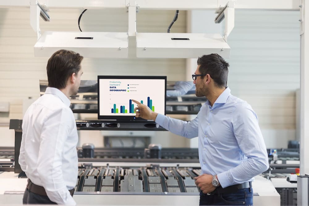Industrial Workforce with Real-time Performance Management through Digital Signage: 2 man in the office using digital signange for performance management